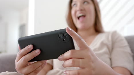 happy plus size biracial woman having smartphone video call in sunny living room, slow motion