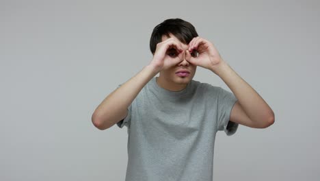 joven con las manos en los binoculares gesto, observando el área alrededor con una mirada seria y atenta, expresando conmoción
