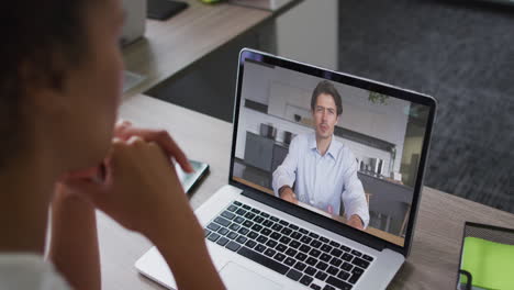 african american businesswoman sitting at desk using laptop having video call with male colleague