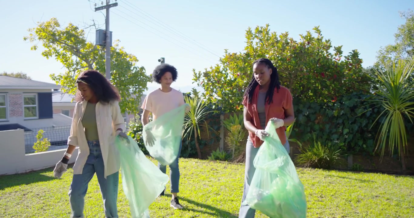 African American friends joining yard cleanup picking up litter with green bags and gloves