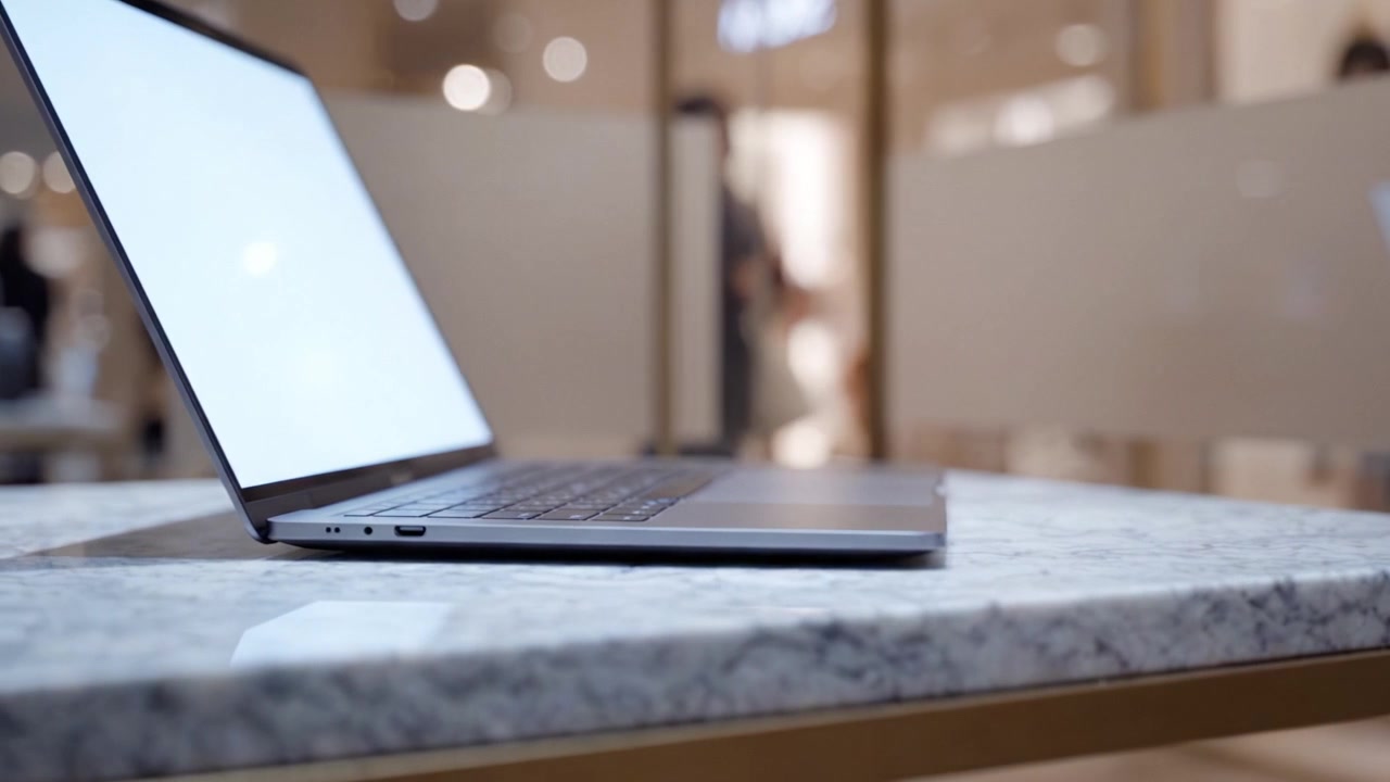 Un elegante laptop poggia su un tavolo di marmo lucido, mostrando il suo design moderno e suggerendo un ambiente vivace sullo sfondo, perfetto per la produttività.