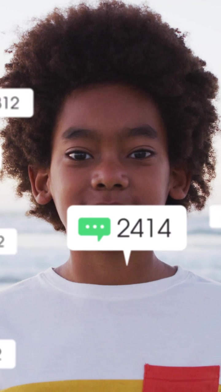 Video verticale: Ragazzo che riceve badge social fluttuanti sul petto, in spiaggia, sorridendo mentre i conteggi aumentano.