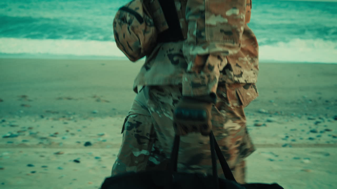 Un soldato americano cammina sulla spiaggia vicino all'oceano con una borsa in mano