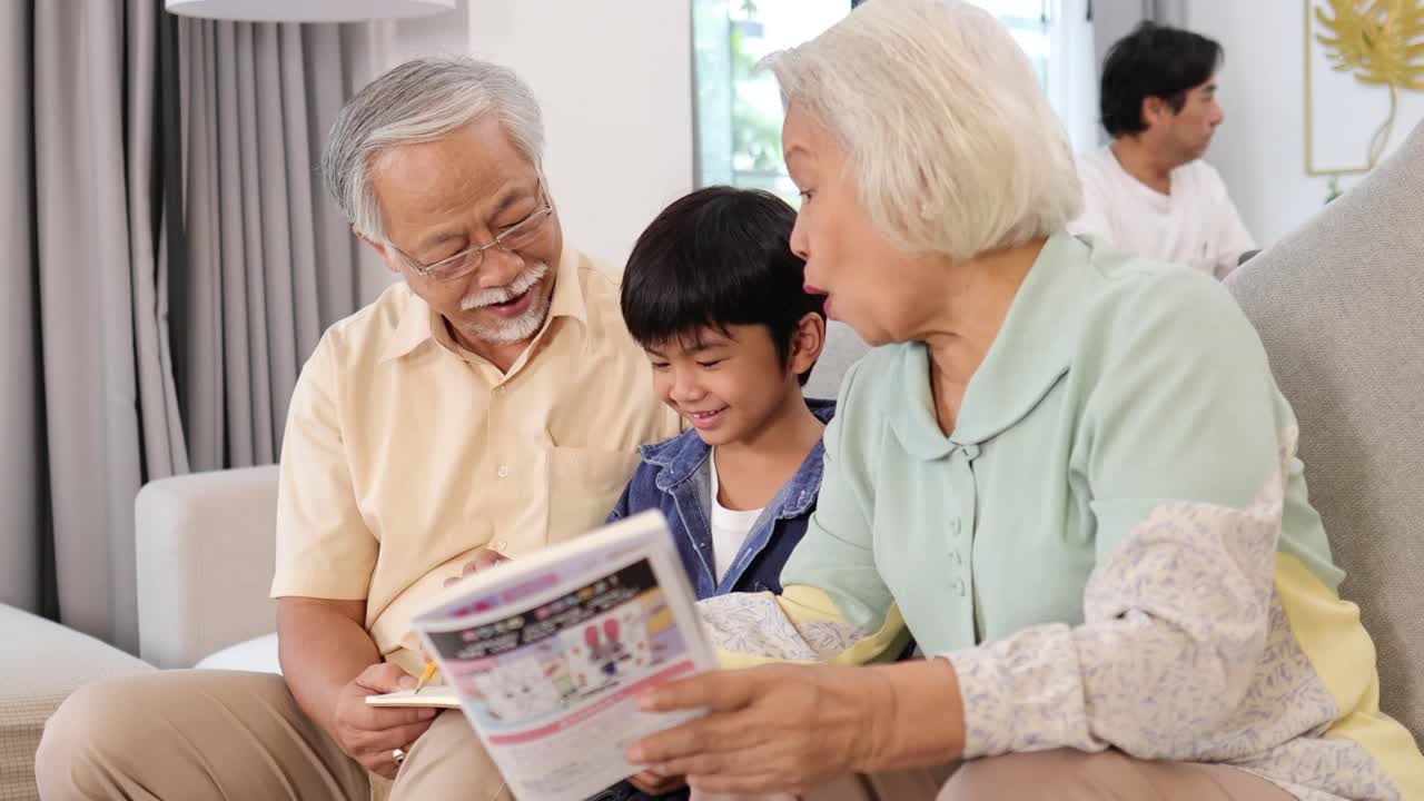 アジア人の祖父母と孫が、居心地の良いリビングルームのソファで一緒に本を読んでいる様子。
