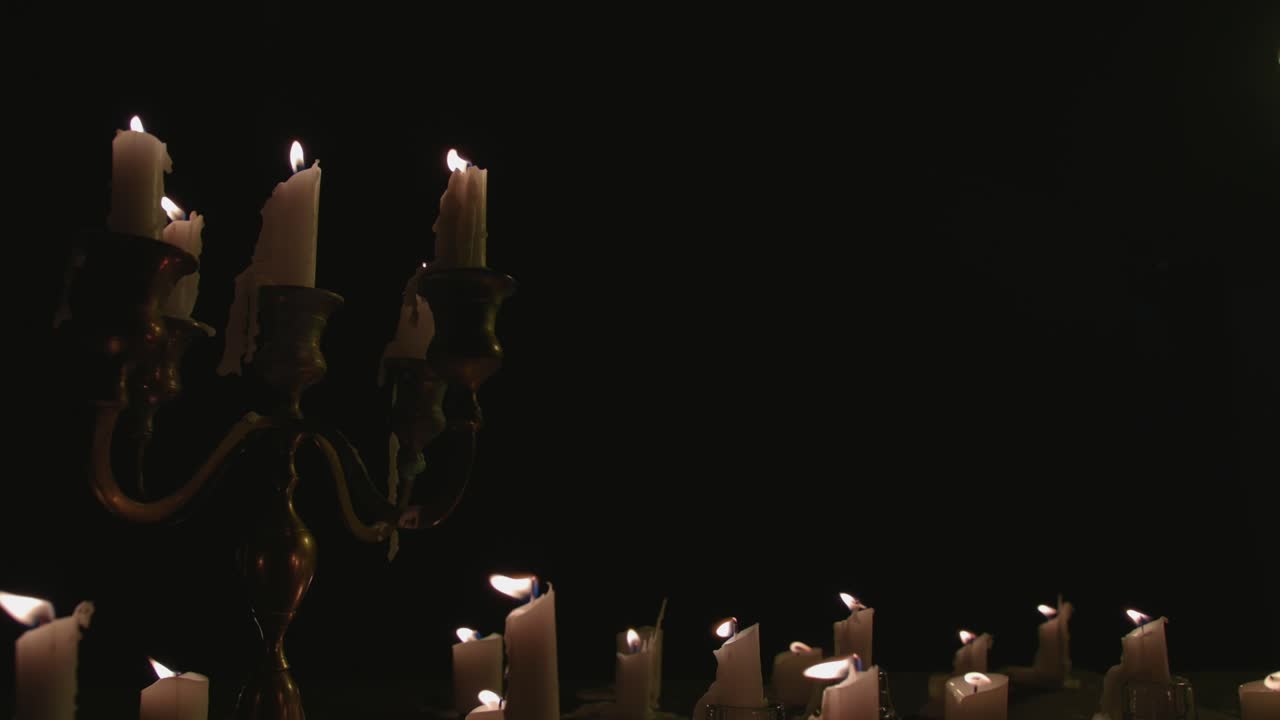 En gruppe hvide stearinlys, nogle på en kandelaber, tændt og brændende i et stykke tid i slowmotion.