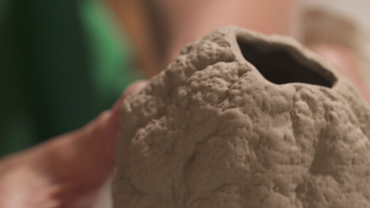 un primer plano de una mano de alfarero sosteniendo y examinando cuidadosamente la escultura de forma ovalada de cerámica. artista inspirado trabajando en el estudio.