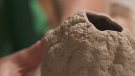 a close-up of a potters hand carefully holding and examining ceramics oval shaped sculpture. inspired artist working in studio.