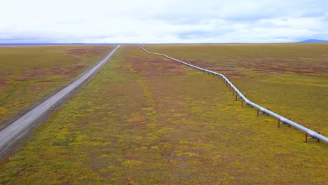 Aerial-view-of-the-Trans-Alaska-Pipeline-System-and-the-North-Slope-Haul-Road,-in-boreal,-fall-color-tundra,-on-a-gloomy,-overcast-day,-in-Alaska,-USA---reverse,-drone-shot