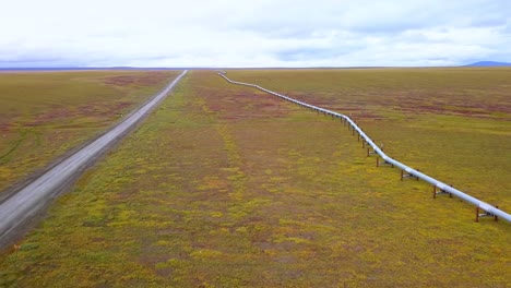 Vista-Aérea-Del-Sistema-De-Oleoductos-Trans-alaska-Y-La-Carretera-De-Acarreo-De-La-Pendiente-Norte,-En-Boreal,-Tundra-De-Color-Otoñal,-En-Un-Día-Sombrío-Y-Nublado,-En-Alaska,-Ee.uu.---Marcha-Atrás,-Disparo-De-Drone