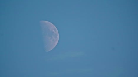 Eine-Noch-Immer-Niedrige-Aufnahme-Des-Mondes-Im-Ersten-Viertel,-Der-Sich-Sanft-Am-Klaren-Blauen-Himmel-Bewegt