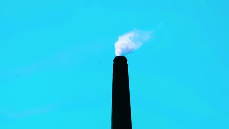 static shot of a tall factory chimney releasing smoke at blue sky background