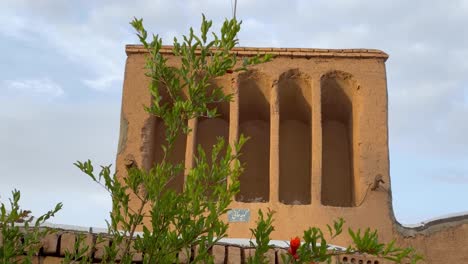 Ländliche-Architektur-Lehmziegelstruktur-Mit-Traditioneller-Musterform-An-Einem-Bewölkten,-Sonnigen-Tag-Wind-Bewegt-Die-Äste-Des-Granatapfelbaums-Rote-Blühende-Blume-Blüht-Im-Frühling-Windfänger