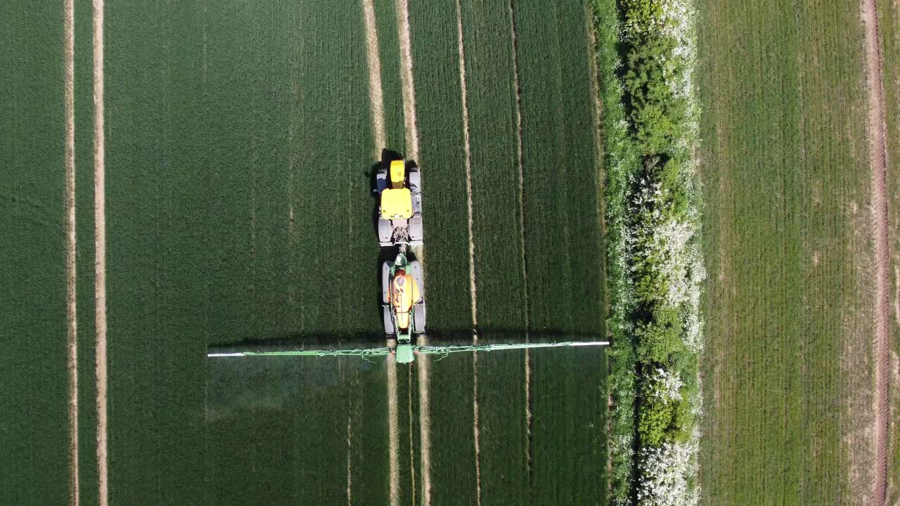un disparo de un dron desde arriba hacia abajo siguiendo un tractor verde y amarillo trabajando en sus campos y rociando sus cultivos