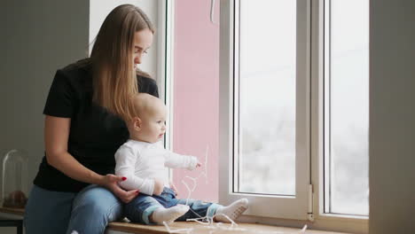 mother and her baby son having fun and playing at home. little kid 1 years old play with his mom arms at home near a big window