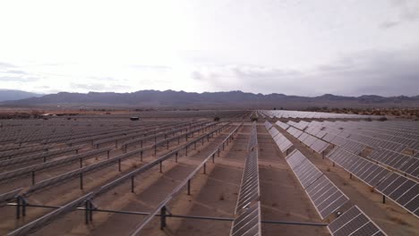 Aerial-panning-view-over-solar-panels-field-with-the-desert-surrounding-it