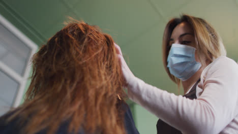 peluquera que usa una máscara facial secando el cabello de una cliente en una peluquería