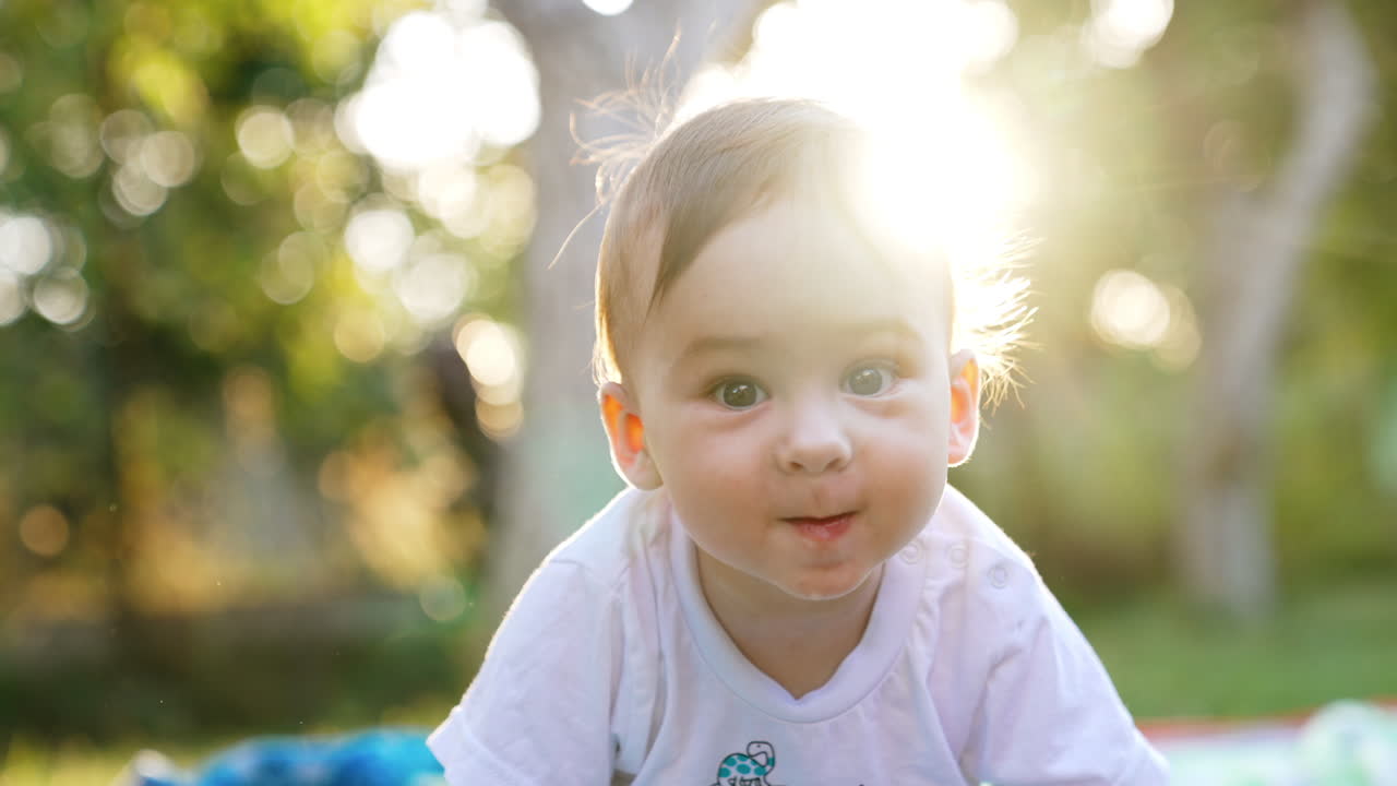 Lovely adorable baby playing in the garden. Cute little kid in the rays of bright sun. Close up. Blurred backdrop.