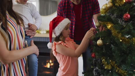 chica caucásica con sombrero de santa decorando el árbol de navidad