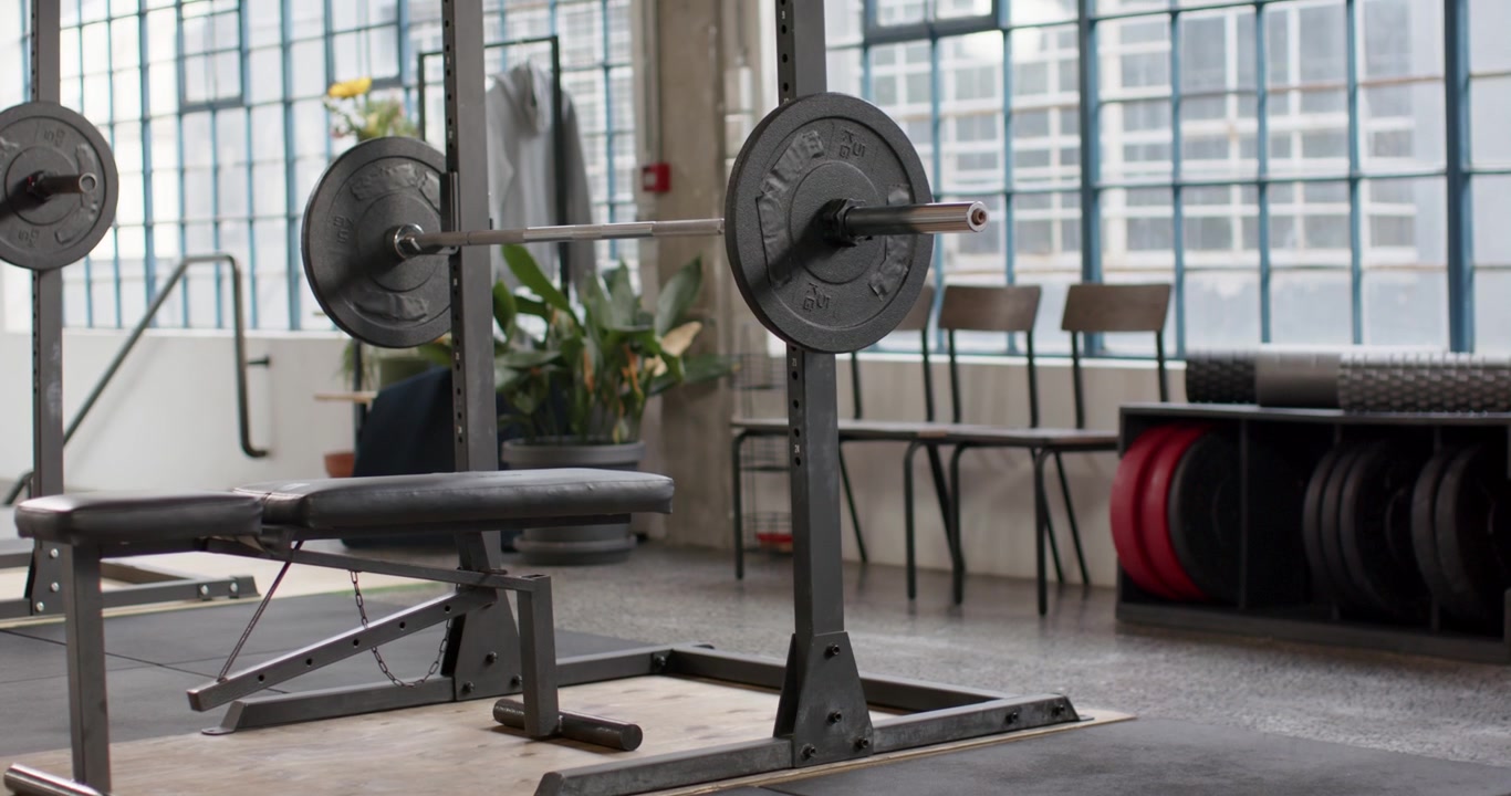 Camera is pulling back and tilting up from low view, revealing loaded barbell and bench centered