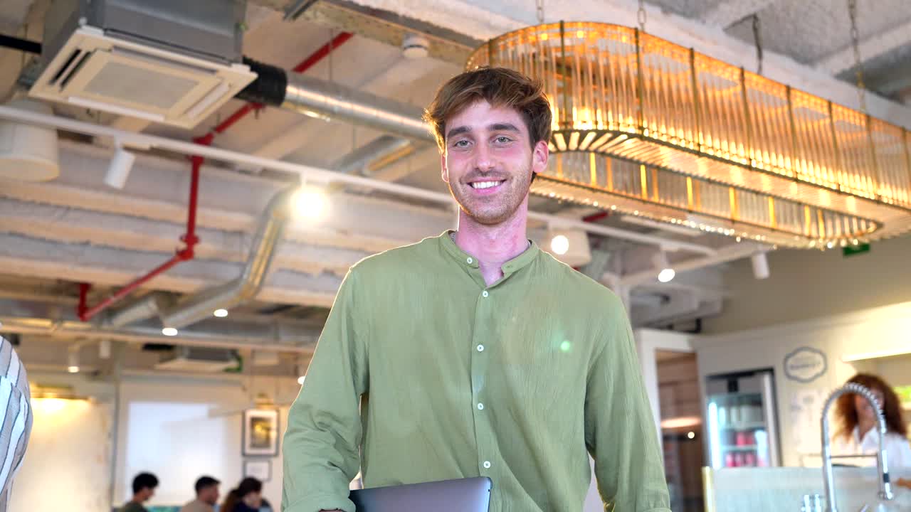 Jovem sorrindo segurando um laptop em um espaço de coworking moderno
