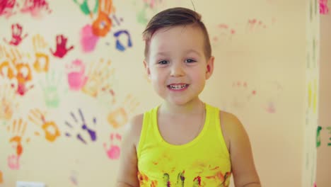 vista de cerca de un niño lindo con manos pintadas después de dejar sus coloridas huellas de manos en la pared y mostrando su pulgar hacia arriba. joven familia feliz. concepto de madre e hijo