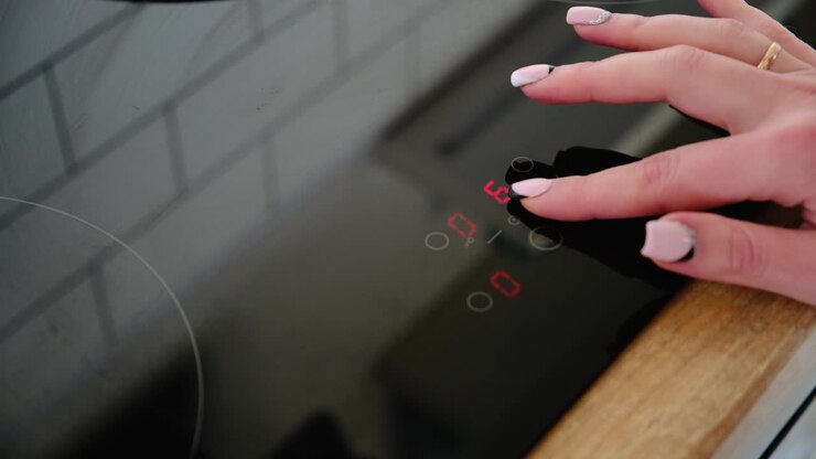 A close-up of a female hand includes an electric stove. Modern technology. Touch panel of electric cooker
