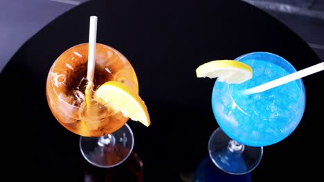 slow orbiting shot showing a blue and an orange freshly made cocktail with garnish