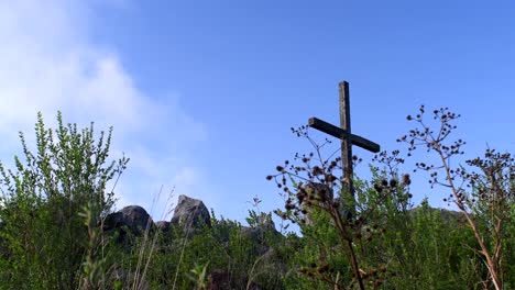 wooden cross on the rocky mountain at sierras de tandil in argentina with wild grasses under the clear blue sky on a windy day - low angle shot