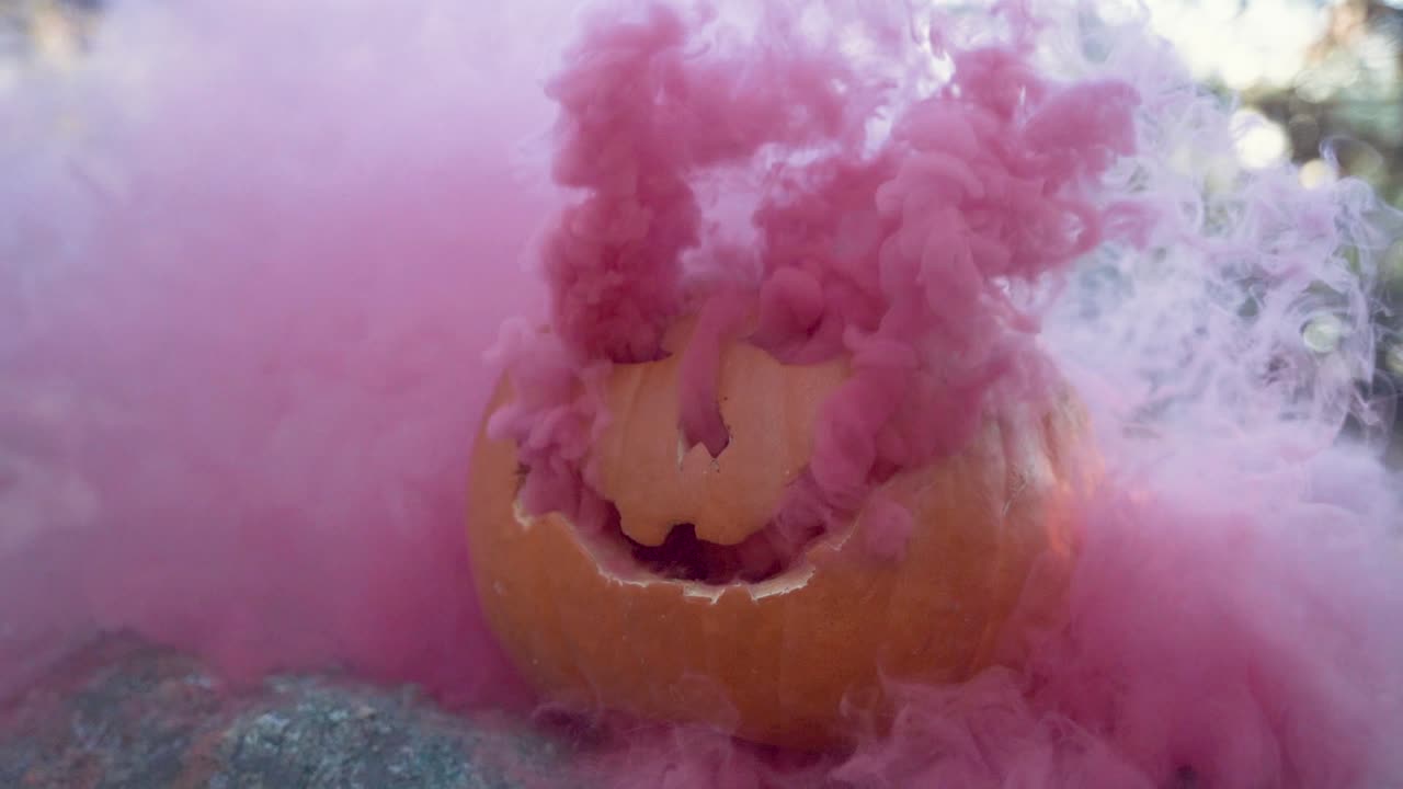 Zucca di Halloween intagliata con fumo rosa che esce dalla faccia da Jack-O'-Lantern per un effetto spettrale al rallentatore, all'aperto nel bosco.