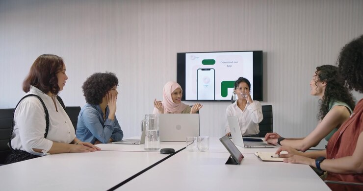 Diverse female colleagues following presenter gestures, giving feedback on app mockup with laptops