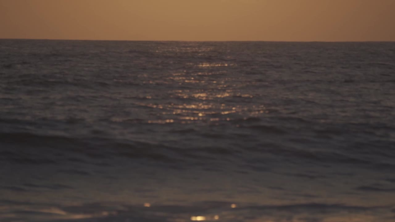 Sunset over the Pacific Ocean of Oaxaca, Mexico. The horizon glows with warm golden and orange hues, reflecting on the gently rippling water, creating a serene and picturesque coastal landscape