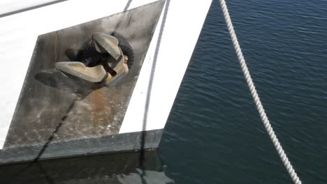 Close-up-of-rusty-metallic-motor-boat-anchor-tied-up-in-dock-with-white-rope-as-water-ripple-and-reflections-pass-by