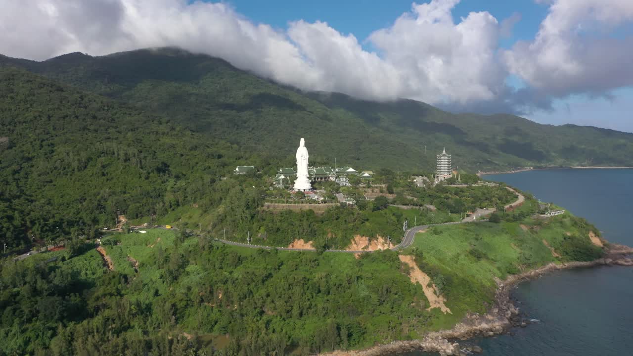 drone aéreo volando hacia la estatua de buda de dama alta y templos con enormes montañas y océano en da nang, vietnam