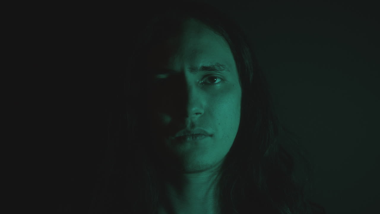 Young Man Opening Eyes and Looking at Camera in Dark Studio