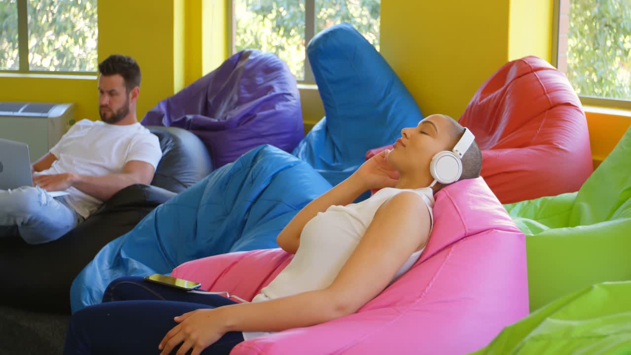 현대적인 사무실 4k에서 휴대 전화로 음악을 듣는 젊은 백인 여성 임원의 측면 뷰