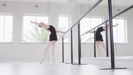 caucasian female ballet dancer stretching up by the mirror in a bright studio