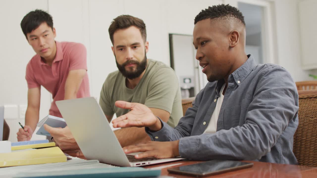 Happy diverse male friends talking and using laptop in living room