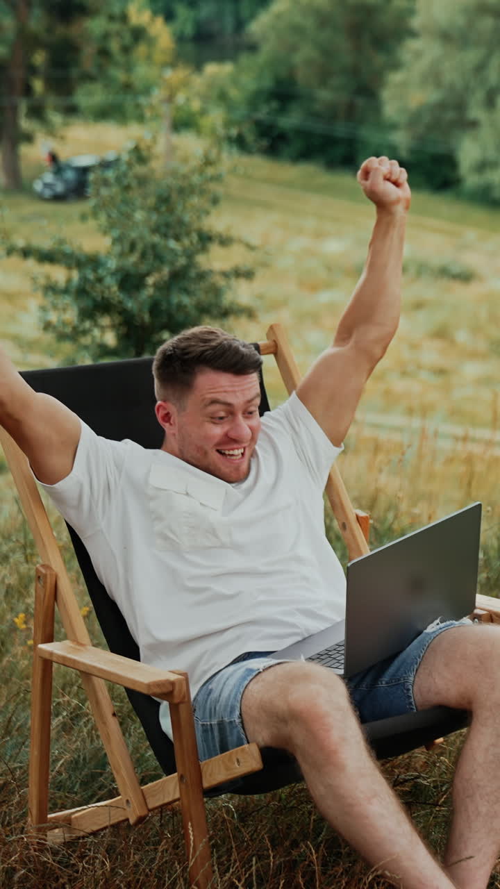 Succeeding at work. Happy Caucasian man rejoices looking at the screen of laptop. Freelancer working in nature. Vertical video