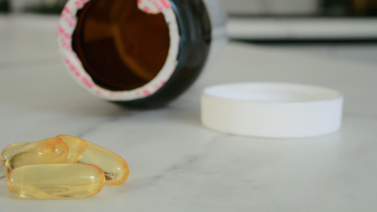 Close up of fish oil supplements scattered on a white table near a pill bottle