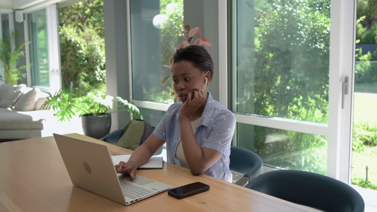 Blue-shirted woman rubbing head, focusing on laptop, typing, studying notebook at home, copy space