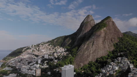 panorámica derecha aérea lenta que muestra los dos picos montañosos de los hermanos en río de janeiro con la favela de vidigal en su fuerte descenso