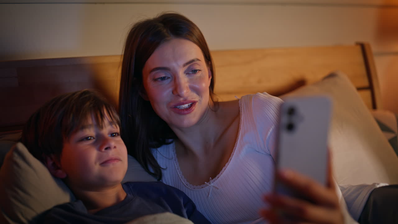 Mom boy videocalling cellphone lying comfortable home bed together closeup