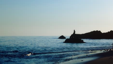 silueta de hombre sentado en una roca en la playa