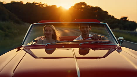 couple driving a classic red convertible at sunset