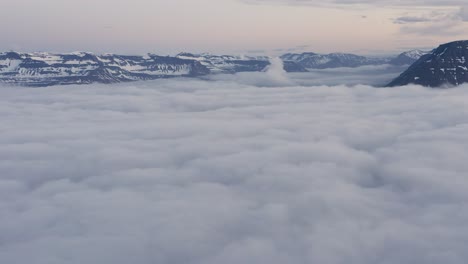 Aerial-above-blanket-of-clouds-with-mountains-peaking-out-in-Icelandic-fjord