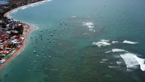 Aerial-drone-wide-shot-of-the-famous-Porto-de-Galinhas-or-Chicken-Port-beach-with-dozens-of-anchored-sailboats-and-hundreds-of-tourists-swimming-in-the-crystal-clear-ocean-water-in-Pernambuco,-Brazil