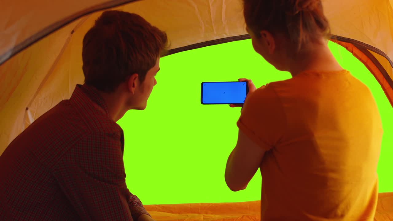 여성이 텐트에서 남자와 함께 앉아있는 동안 전화로 사진을 찍습니다.모크업에 대한 chromakey. 여성은 텐트 안에서 남자와 함께 전화를 들고 있습니다. 그린 스크린. 커플 사랑