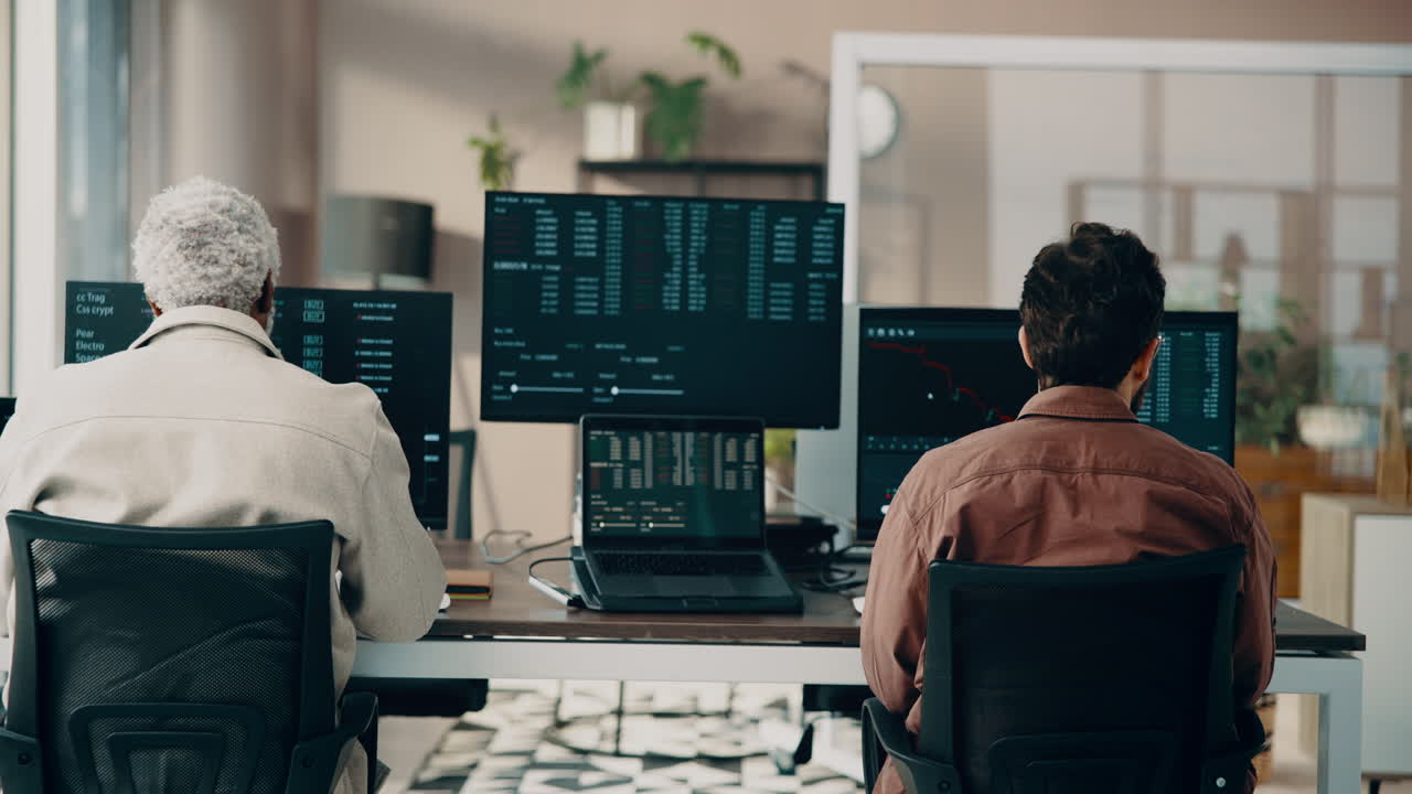 Two men working on computers analyzing stock market data