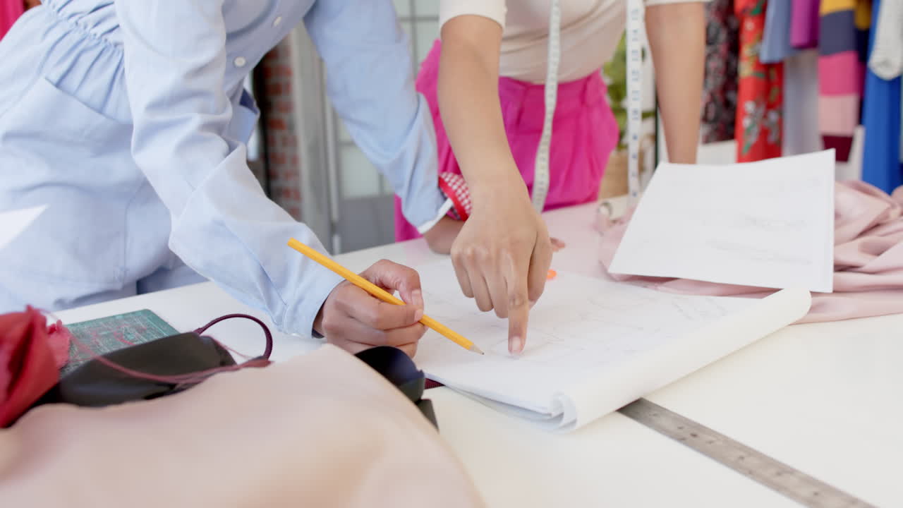 sección media de diversas diseñadoras de moda discutiendo diseño en la mesa en el estudio, cámara lenta