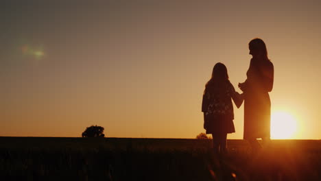 a woman with a girl admires the beautiful sunset in a picturesque place silhouettes of mom and daugh